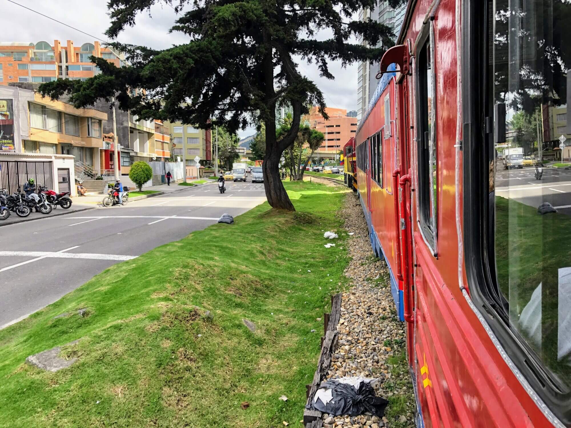 Red carriages of the Tren de la Sabana traveling beside a city street in Bogotá, Colombia.