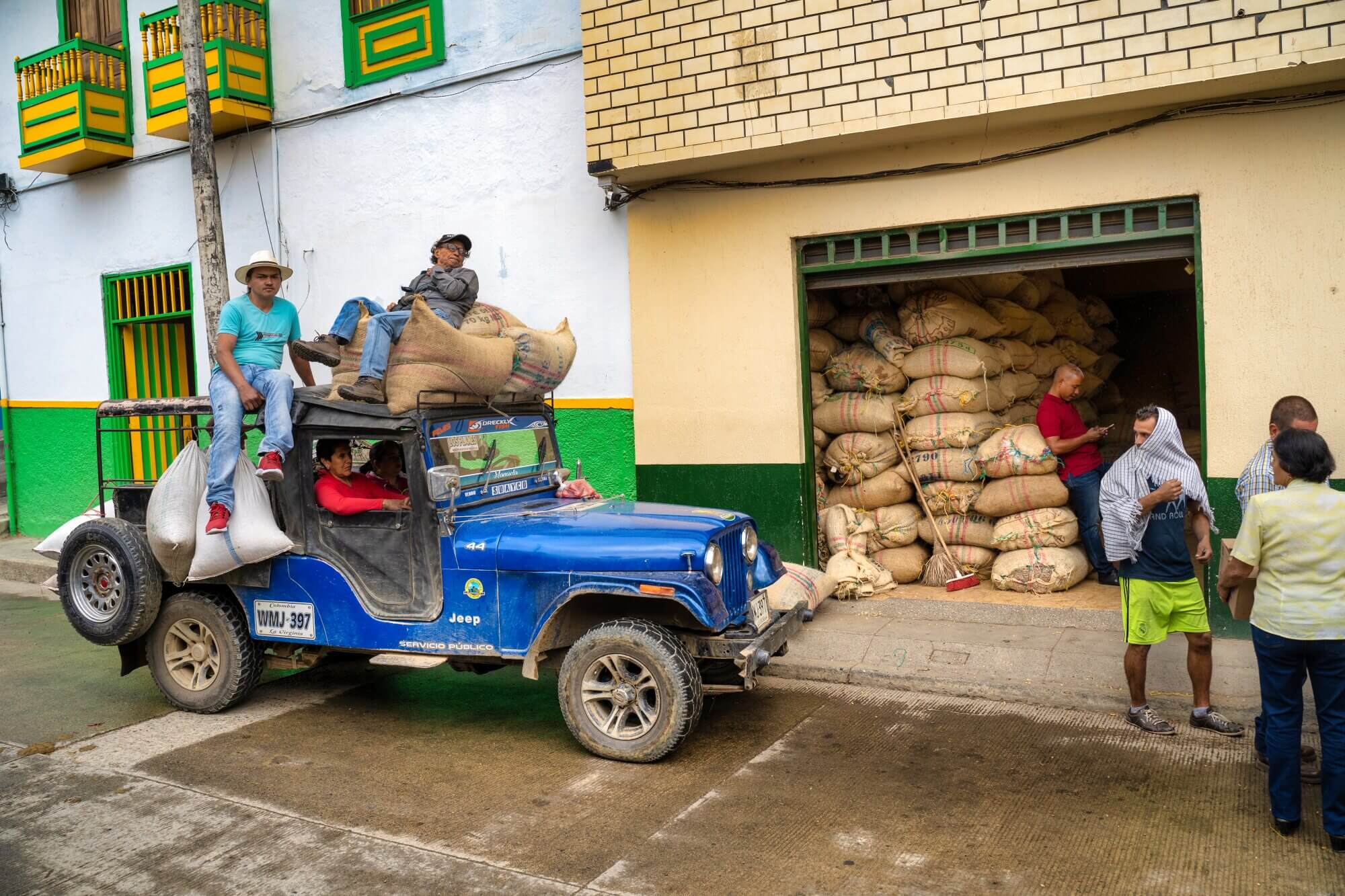 Blue Willys Jeep loaded with sacks of coffee outside a warehouse in Colombia’s coffee region.