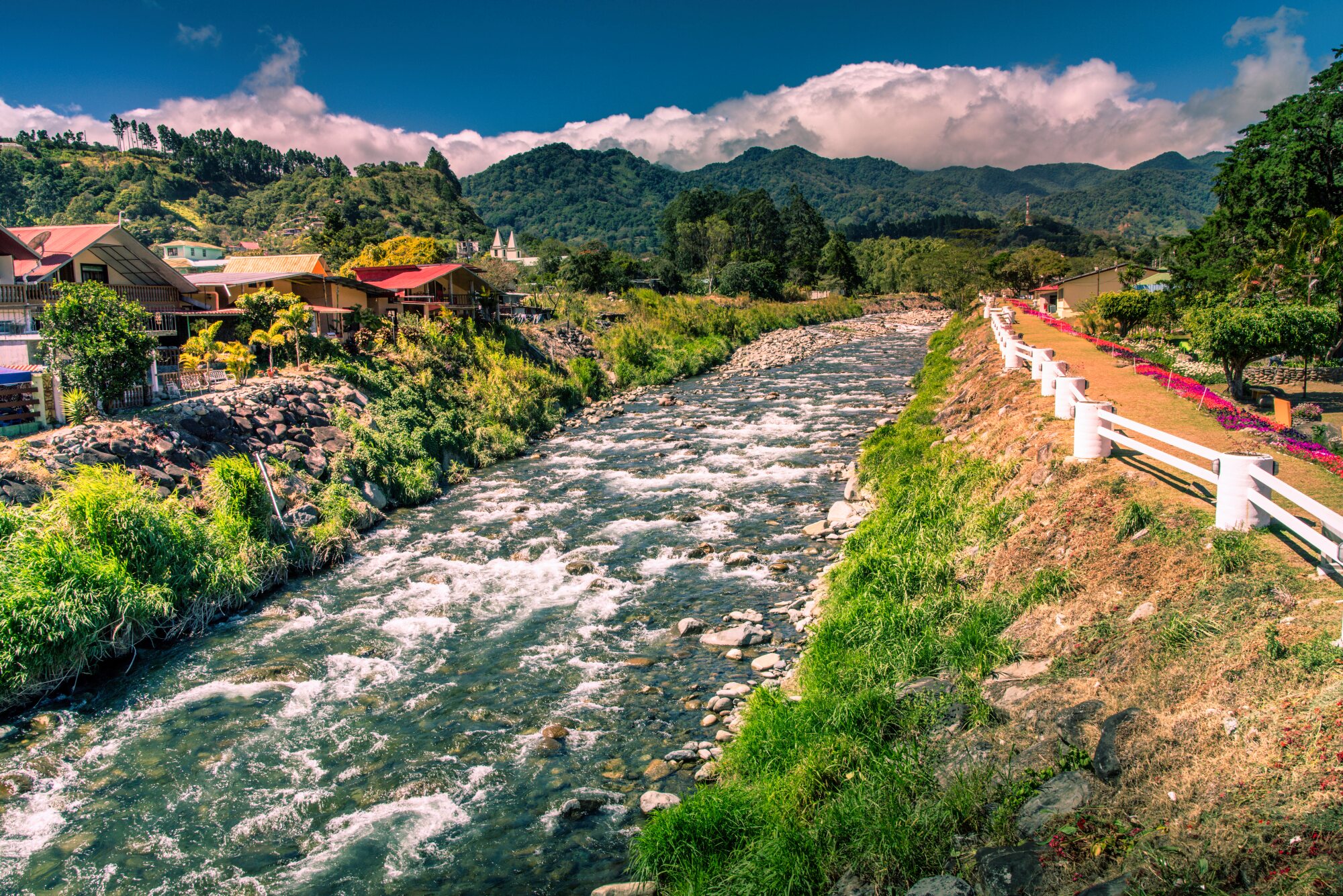 Mountain river flowing through Boquete with gardens, houses and forested hills in the background.