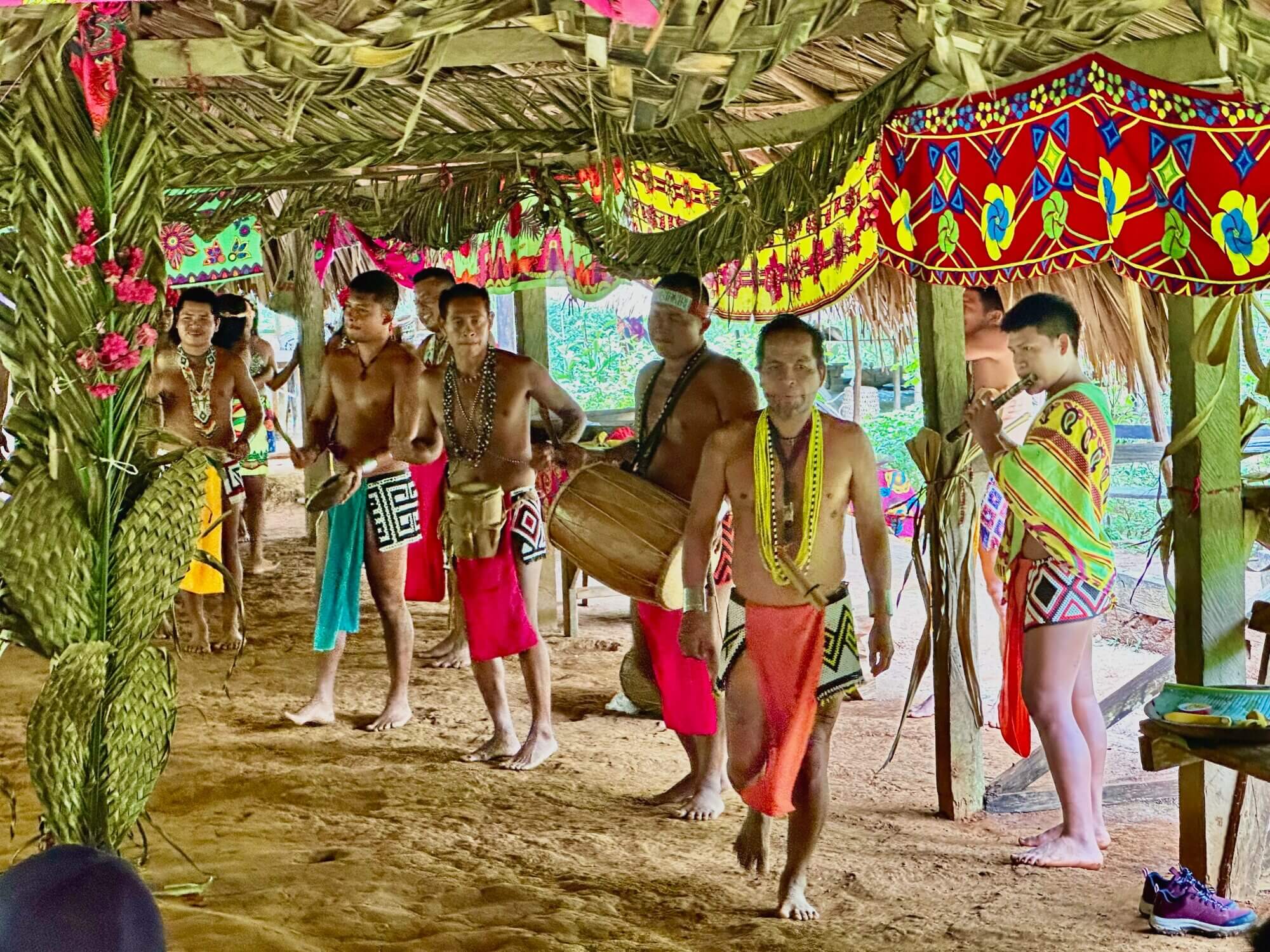 Emberá musicians playing drums and flute beneath a thatched shelter in Panama.