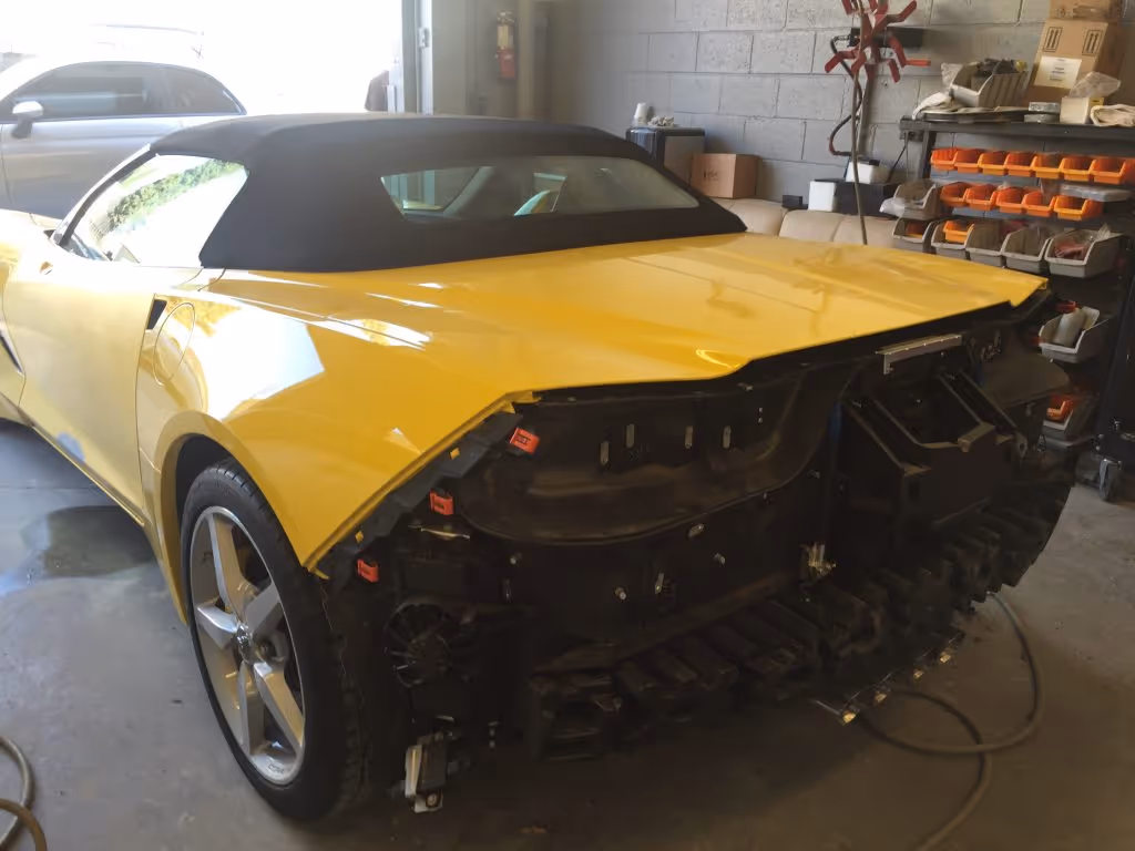 Yellow convertible car with black soft top missing its rear bumper and taillights parked inside a garage.
