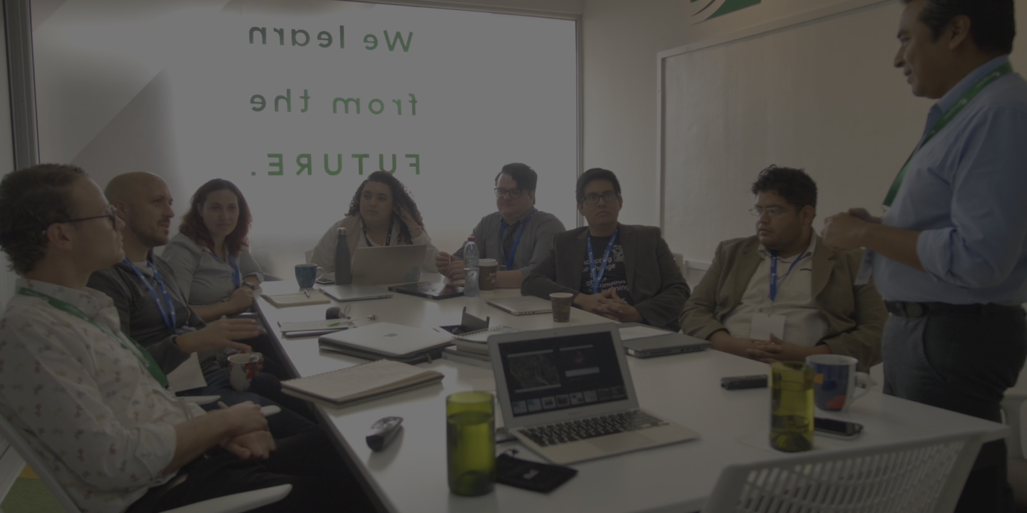 Person with long blonde hair working at a large table covered with cardboard templates in a spacious industrial workshop.