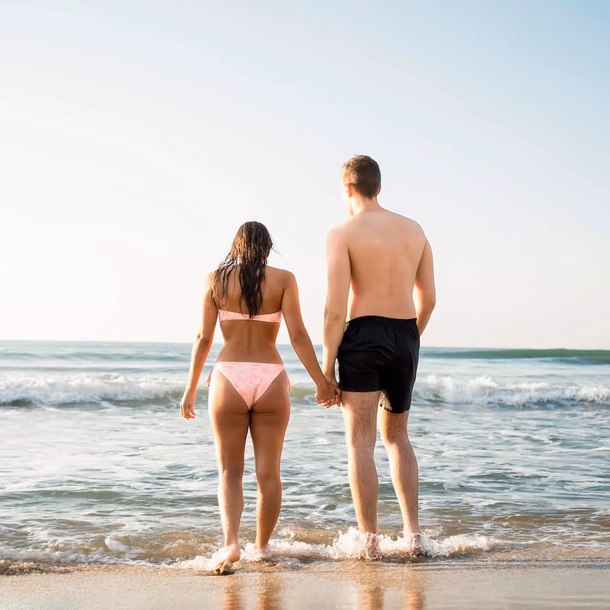 Couple holding hands while walking into the ocean, representing confidence after body contouring treatment