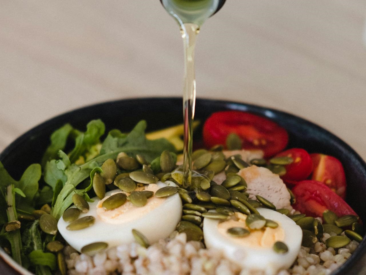 a healthy salad bowl with vegetables, eggs and seeds, olive oil being poured on it