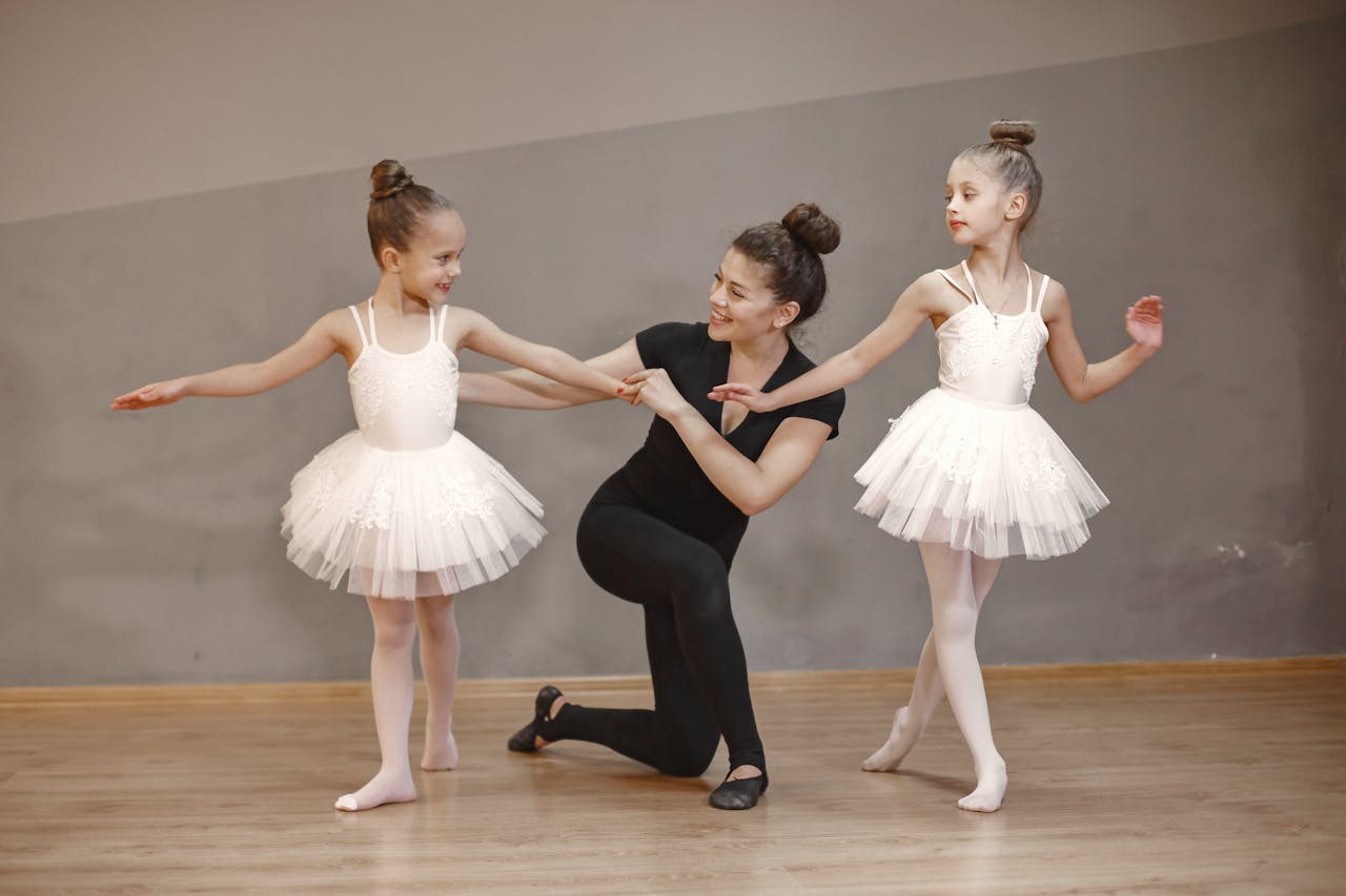 a teacher teaching ballet to two young girls, smiling at one of them