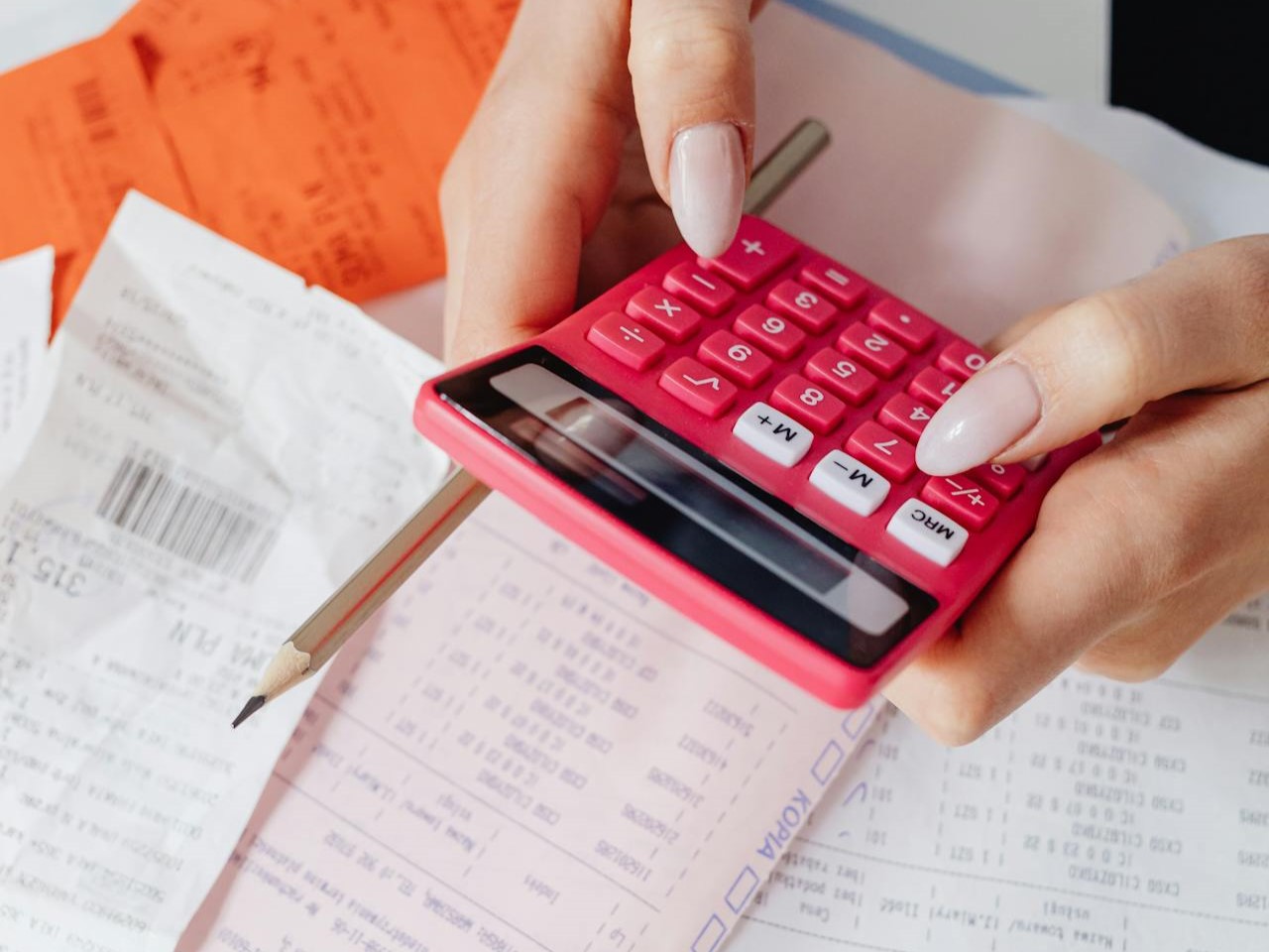 a person using a calculator, pencil in their hand, bills strewn on the table under