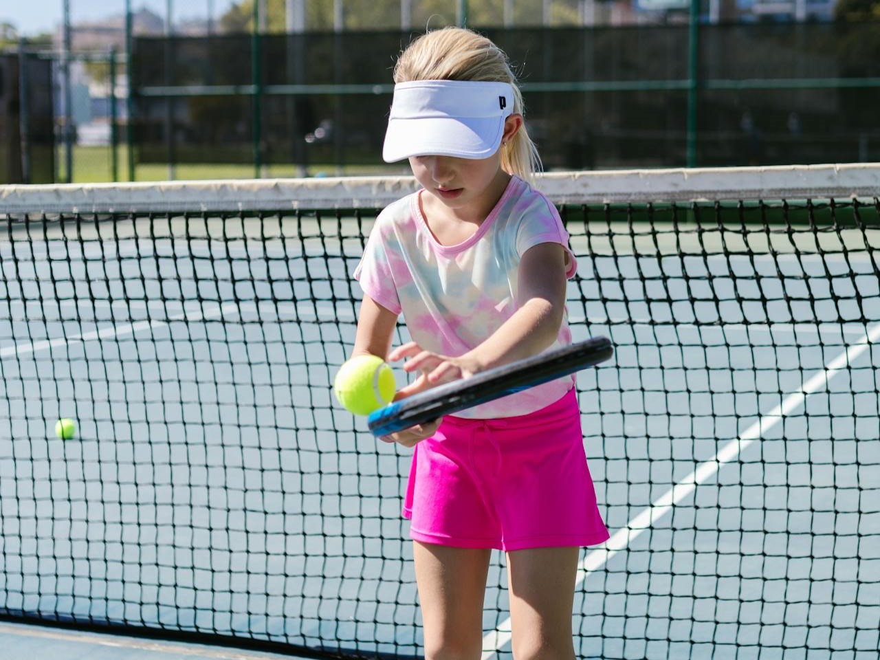a young girl on a tennis court bouncing a ball off a tennis racquet