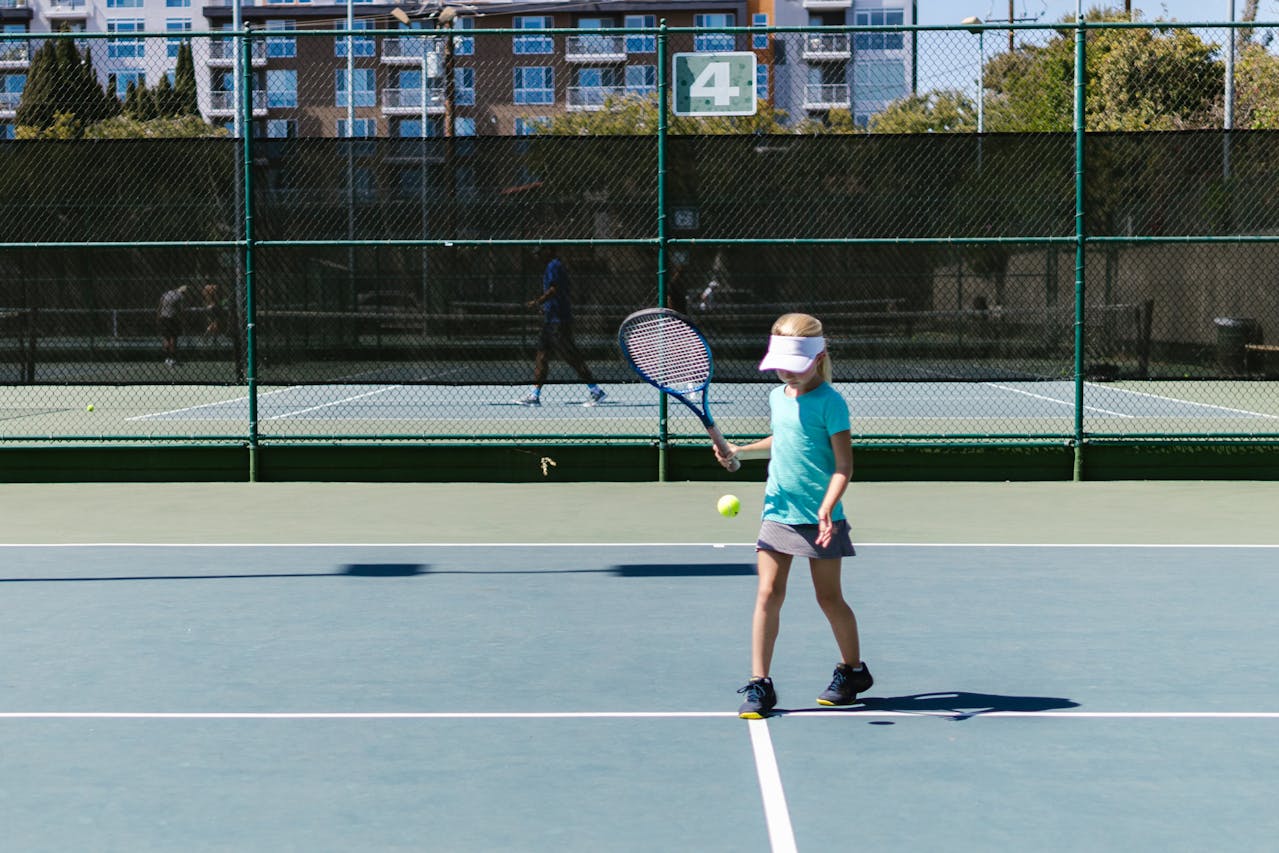 a young girl at tennis coaching, in the midst of hitting the ball with her racquet