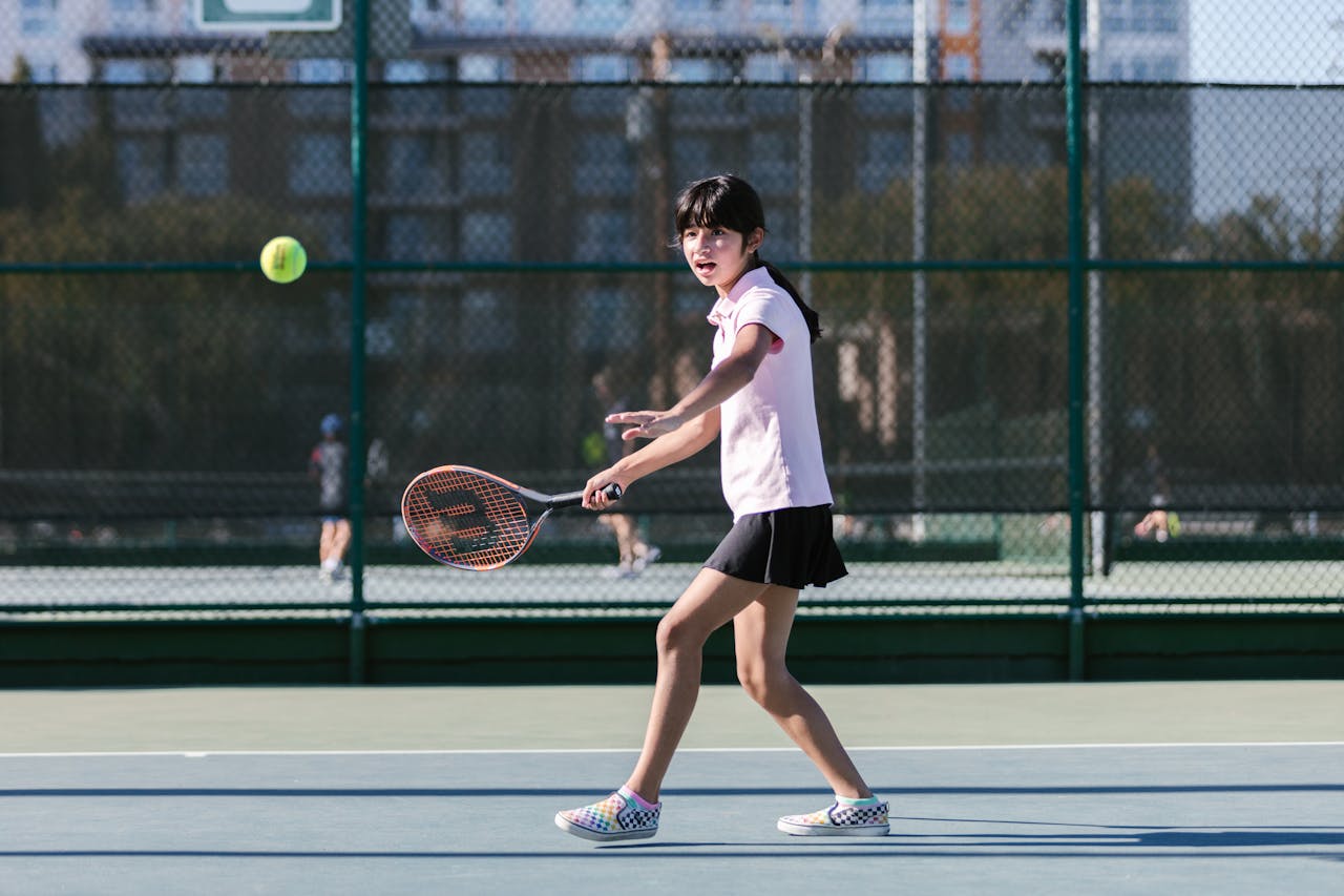 a young girl on a tennis court hitting a ball with a tennis racquet