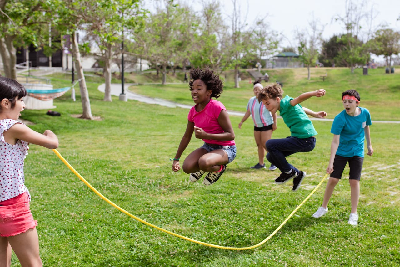 a bunch of kids playing with a skipping rope in a park