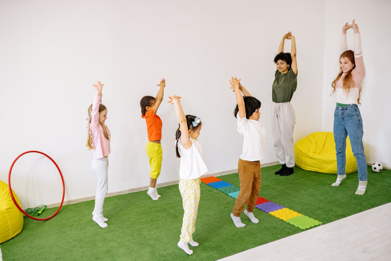 a group of young kids mirrroring their two teachers stretching their arms above their heads