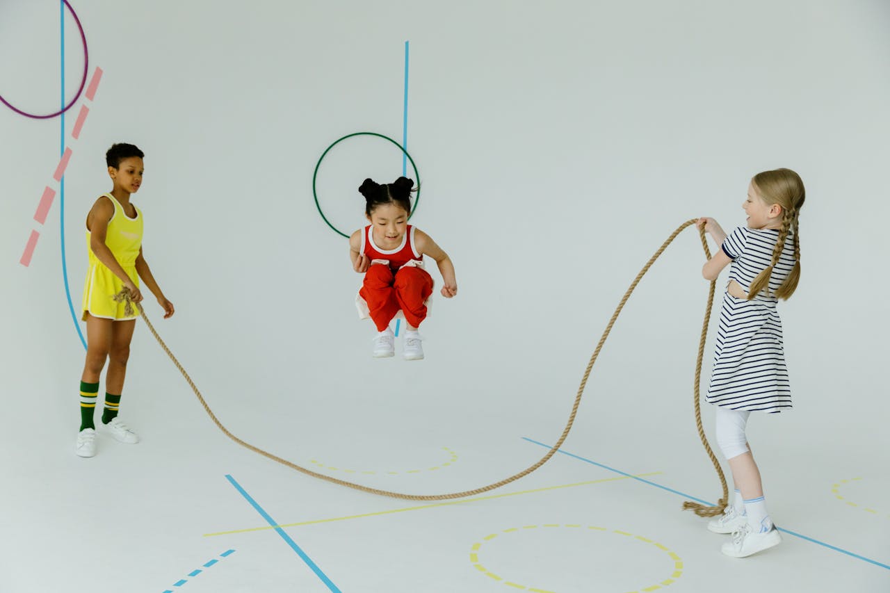 two children holding a skipping rope while one young girl jumps over it