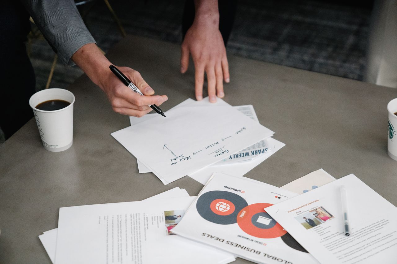 a person drafting a business plan on paper, other printouts and documents spread around them on the table