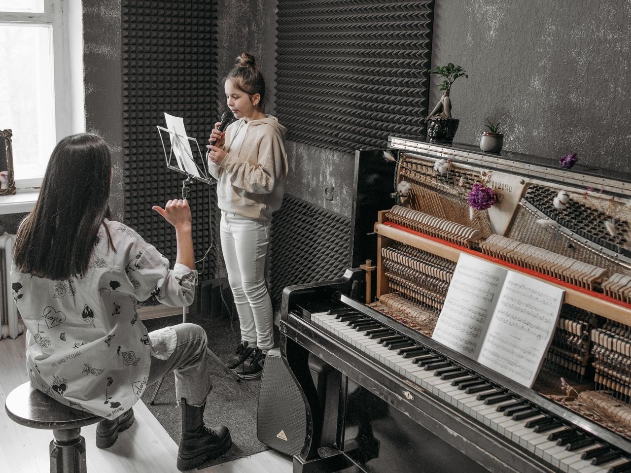 a young girl taking vocal music lessons from a music teacher, a keyboard with sheet music to their left