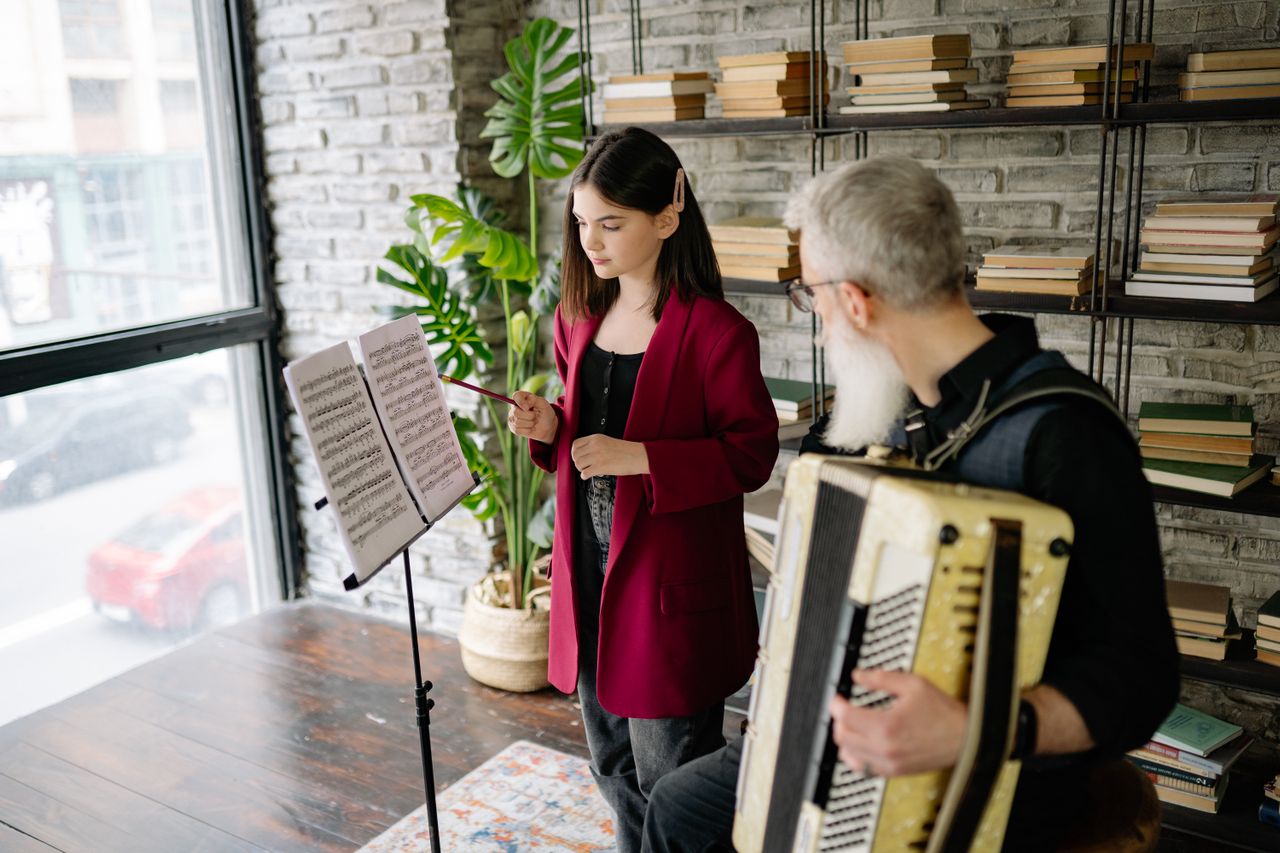 a young girl reading sheet music in her music lesson while her teacher plays the piano accordion