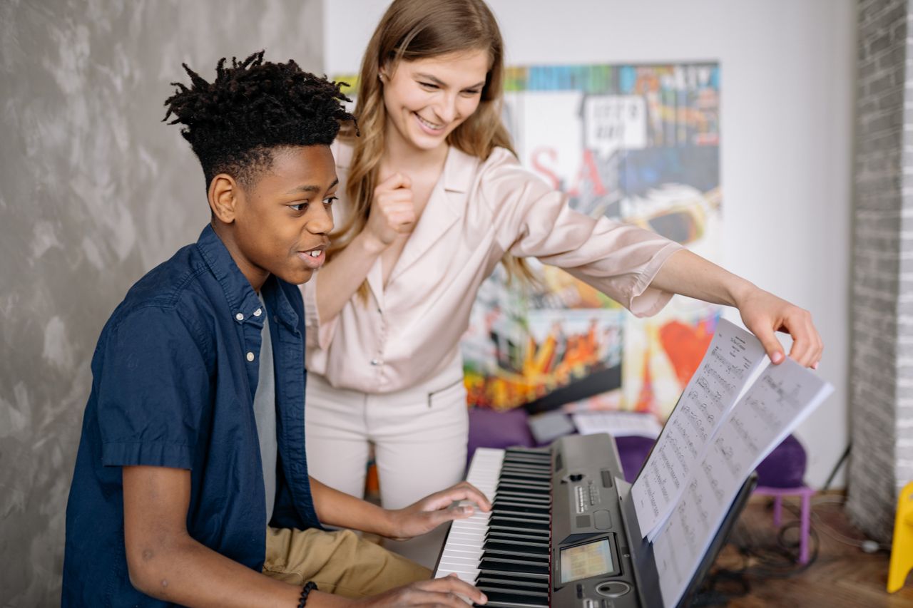 a music teacher smiling at her student who is playing the keyboard