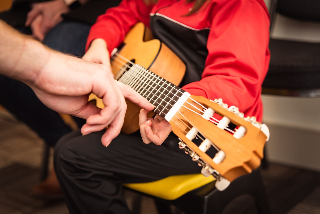 a teacher pointing at a student's guitar string at a music lesson