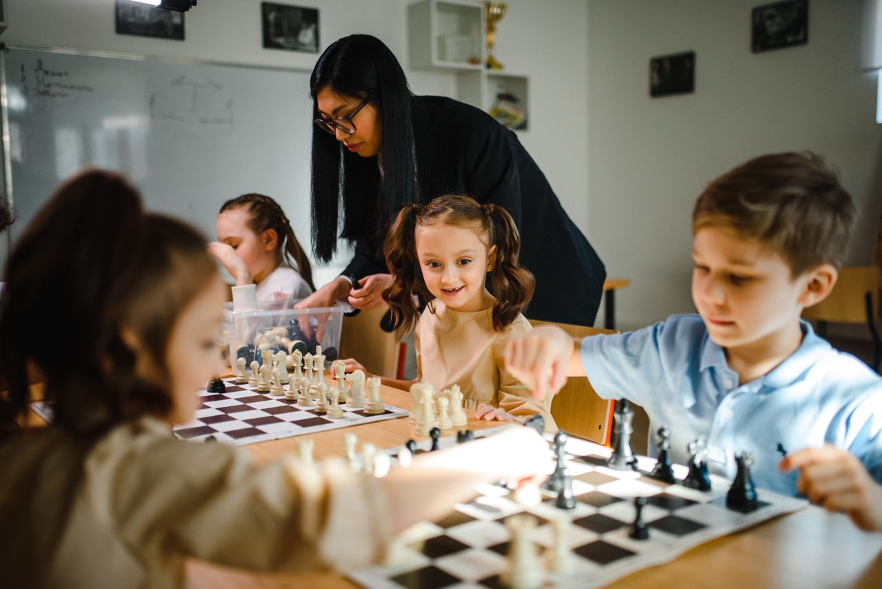 kids playing chess in an after-school activity program, a teacher supervising them