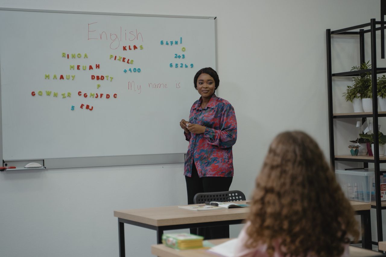 a teacher at a language school explaining English concepts to a student in a classroom setting with a whiteboard.