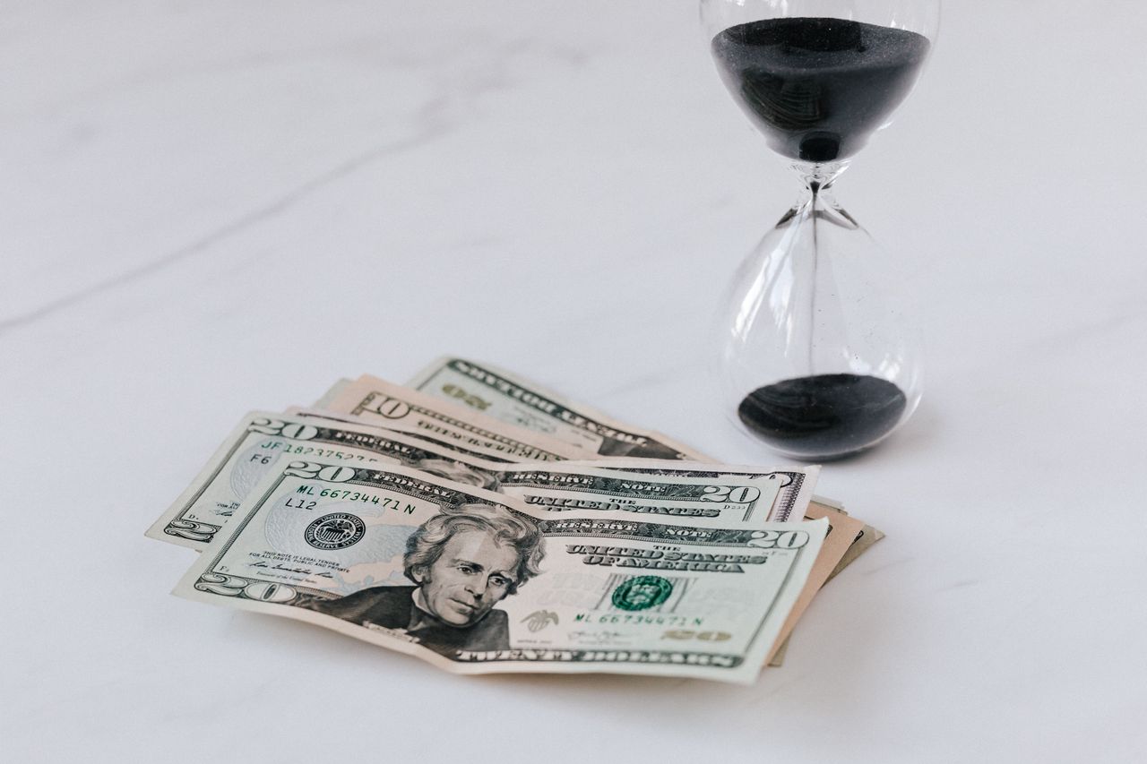 an hourglass with some 20 dollar bills next to it, on a table