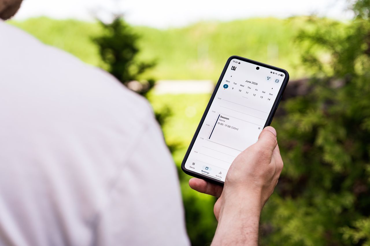 A person using a booking app on a smartphone outdoors, surrounded by greenery.