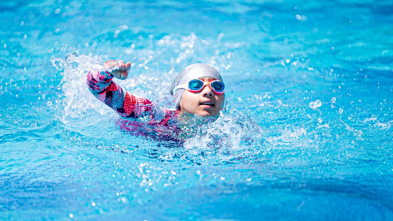 A young swimmer in goggles and cap performing the freestyle stroke in a vibrant blue pool.