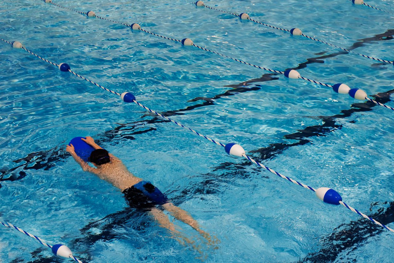 A young swimmer practicing with a kickboard in a swimming pool.