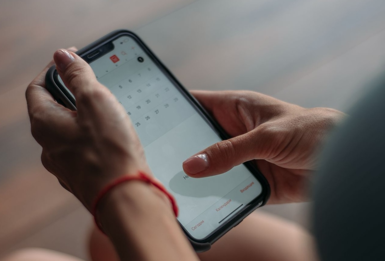Close-up of a person using a smartphone to access the calendar app indoors.  