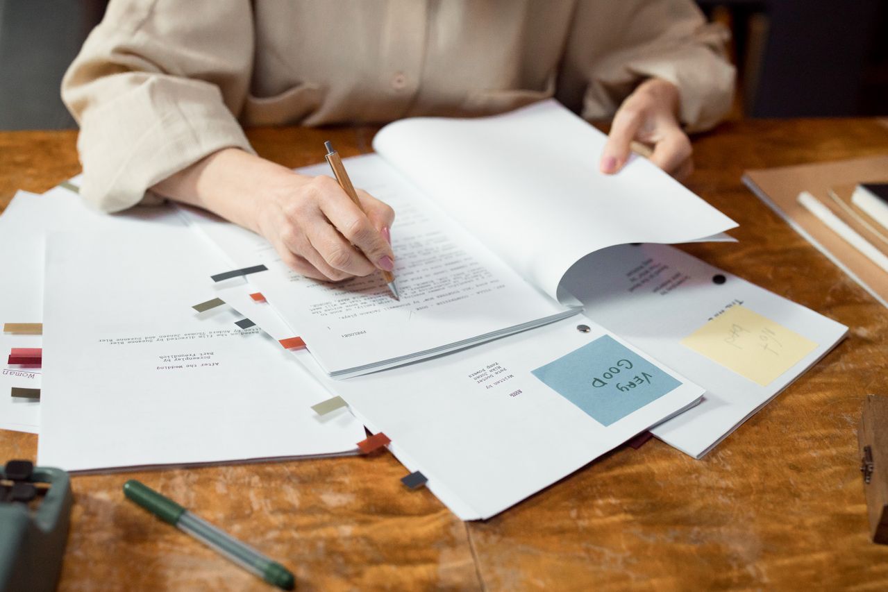 Close-up of a teacher writing, grading and organizing documents on a wooden desk.