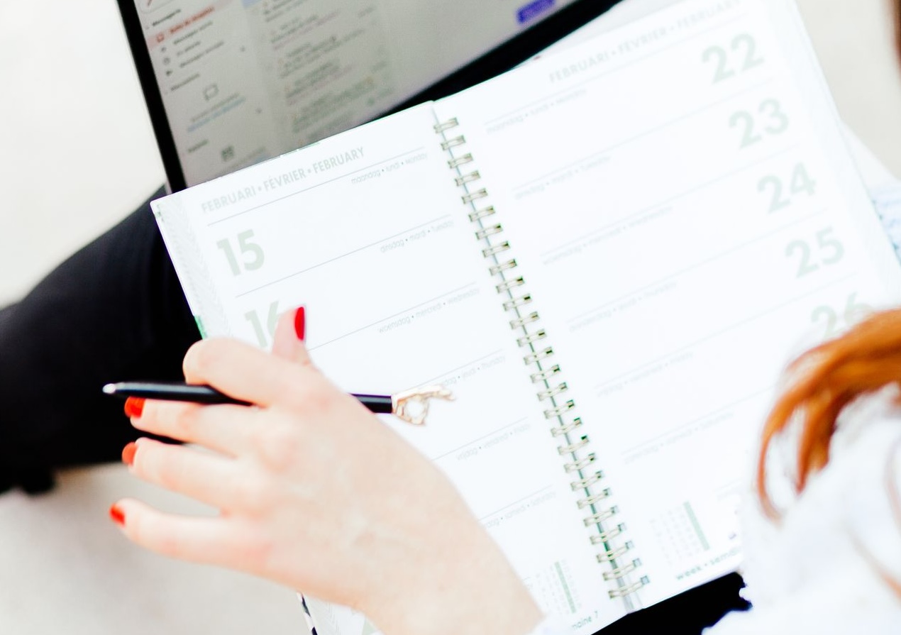 Woman using laptop and notebook for work organization and schedule planning indoors.