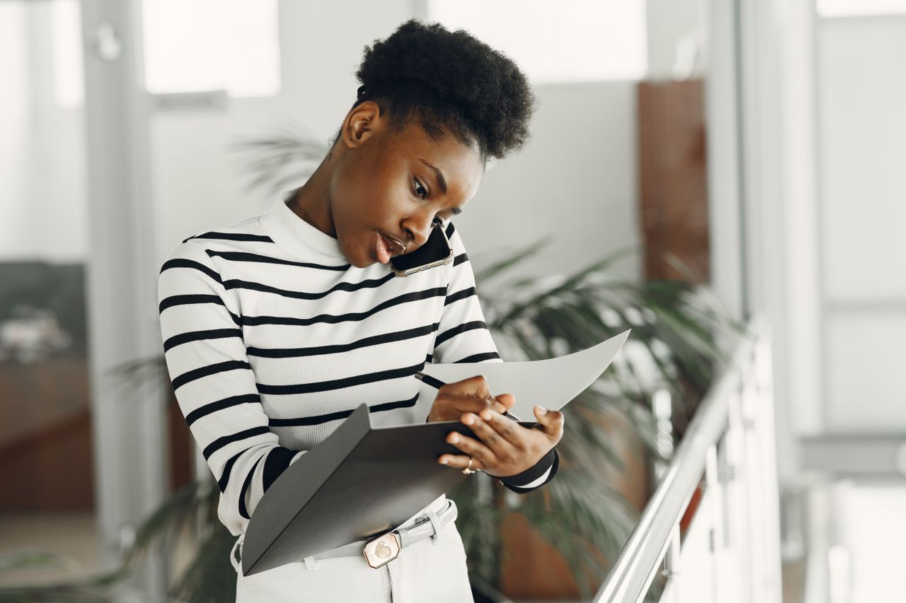 a woman wearing a striped top, talking on the phone while taking notes on a notepad, indoors