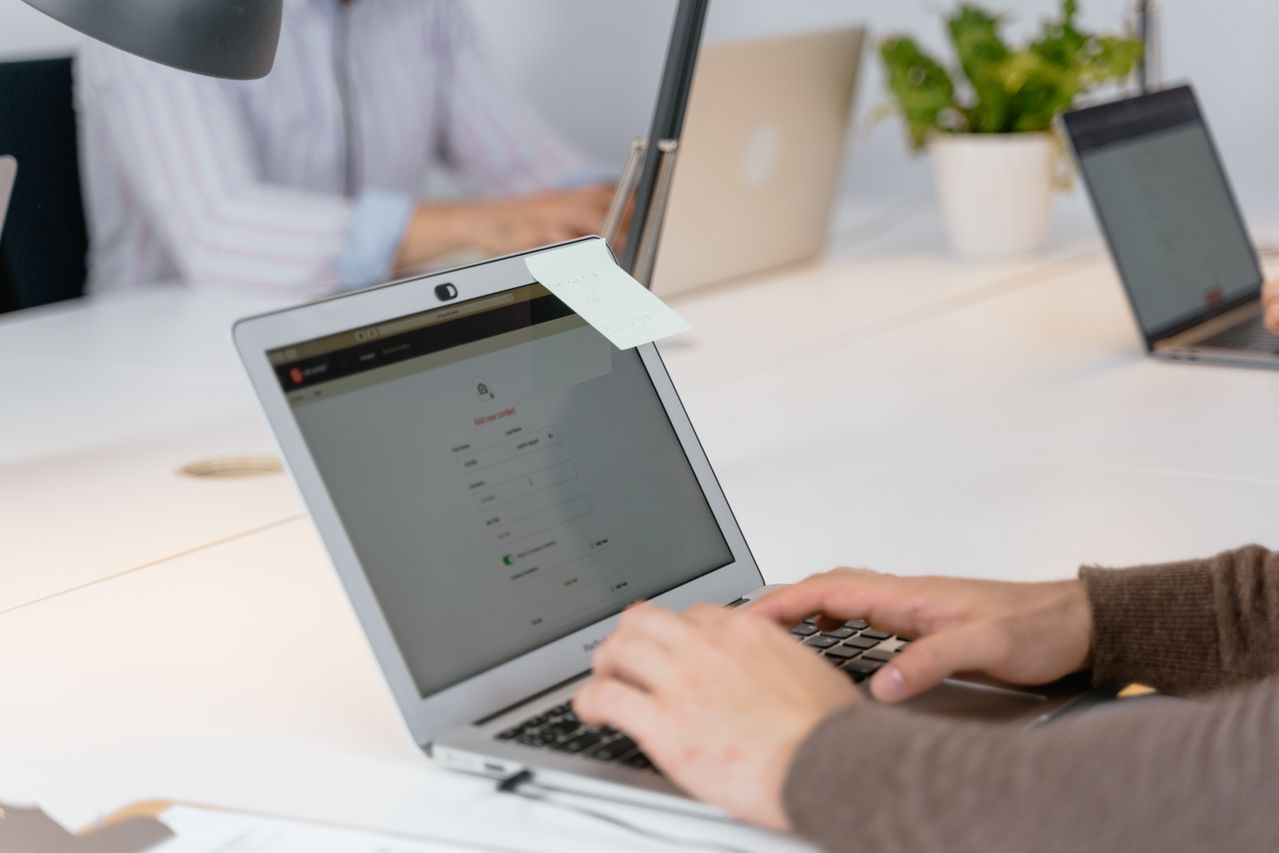 Close-up of a person filling out a lead form on a laptop, with a sticky note on it, in a modern office setting.