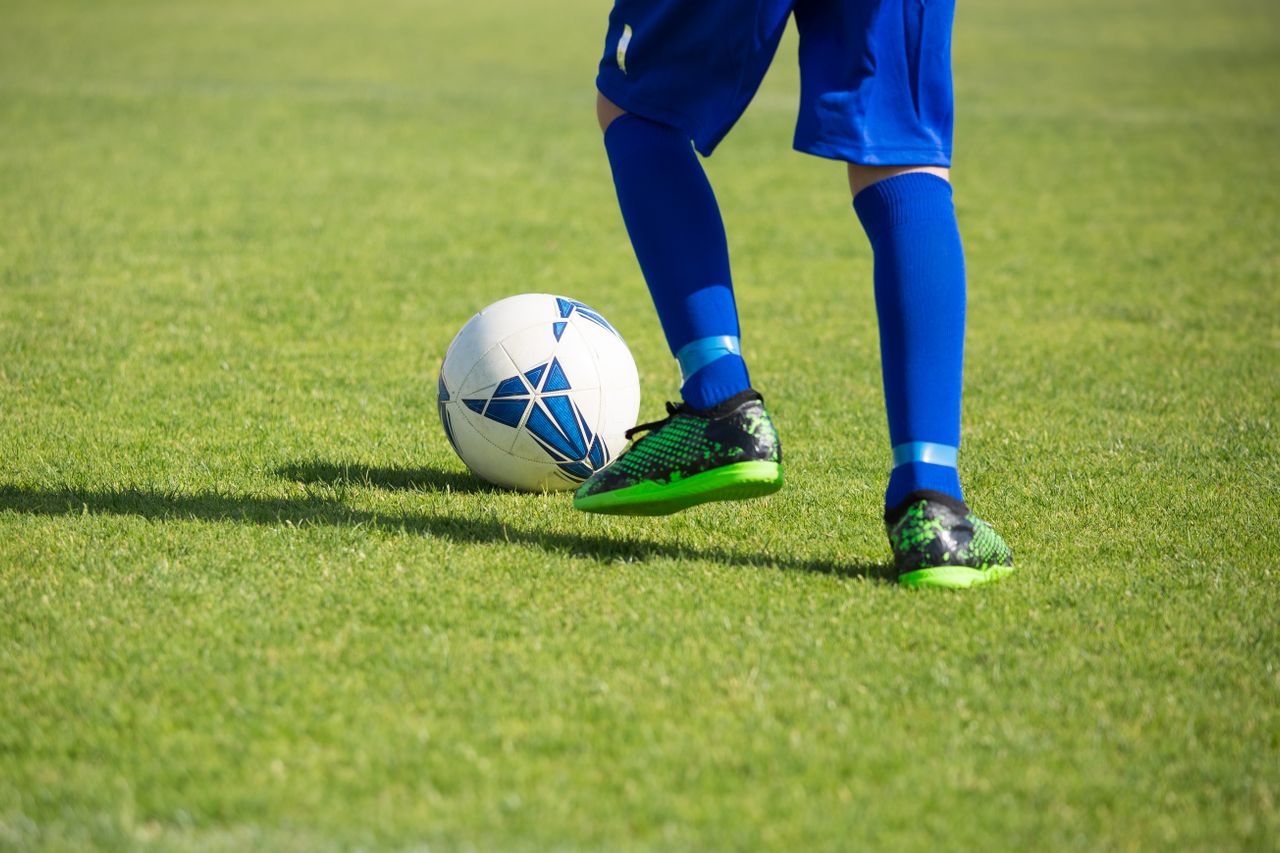 Close-up of a soccer player dribbling a ball on a vibrant green field.