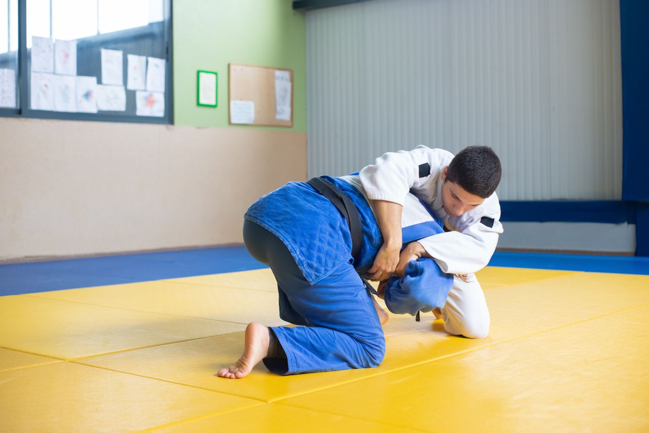 Two men practicing judo techniques on a dojo mat indoors.