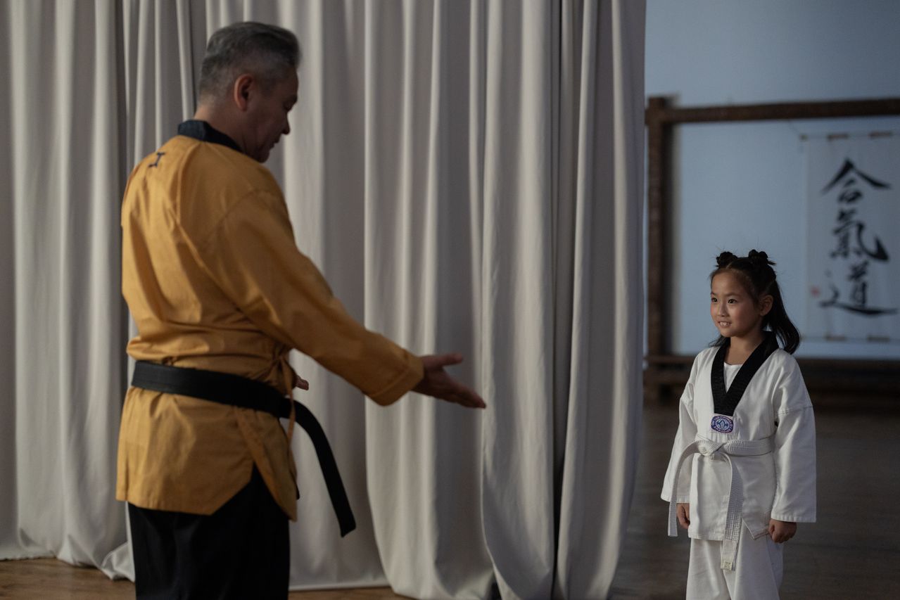 Young girl in karate gi with instructor. Martial arts training in a dojo.