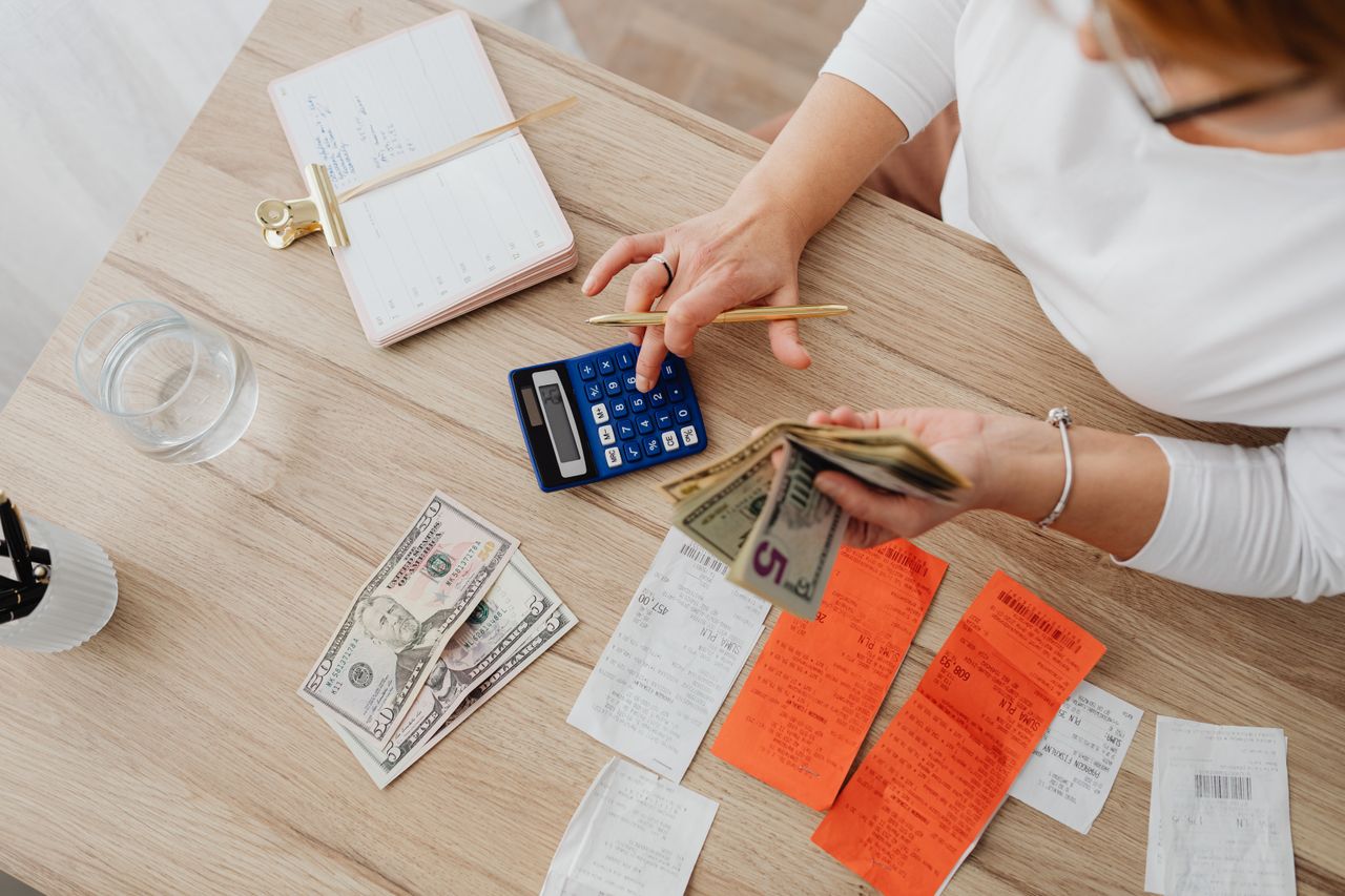 Overhead view of a person using a calculator and notebook to manage cash and receipts at a desk.