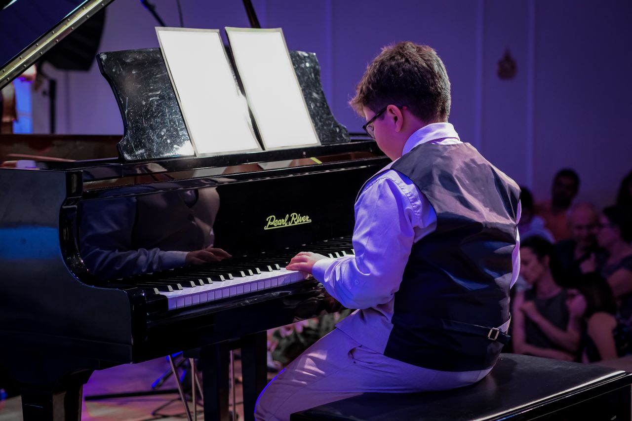 A young boy playing the grand piano during a recital, showcasing his musical talent.