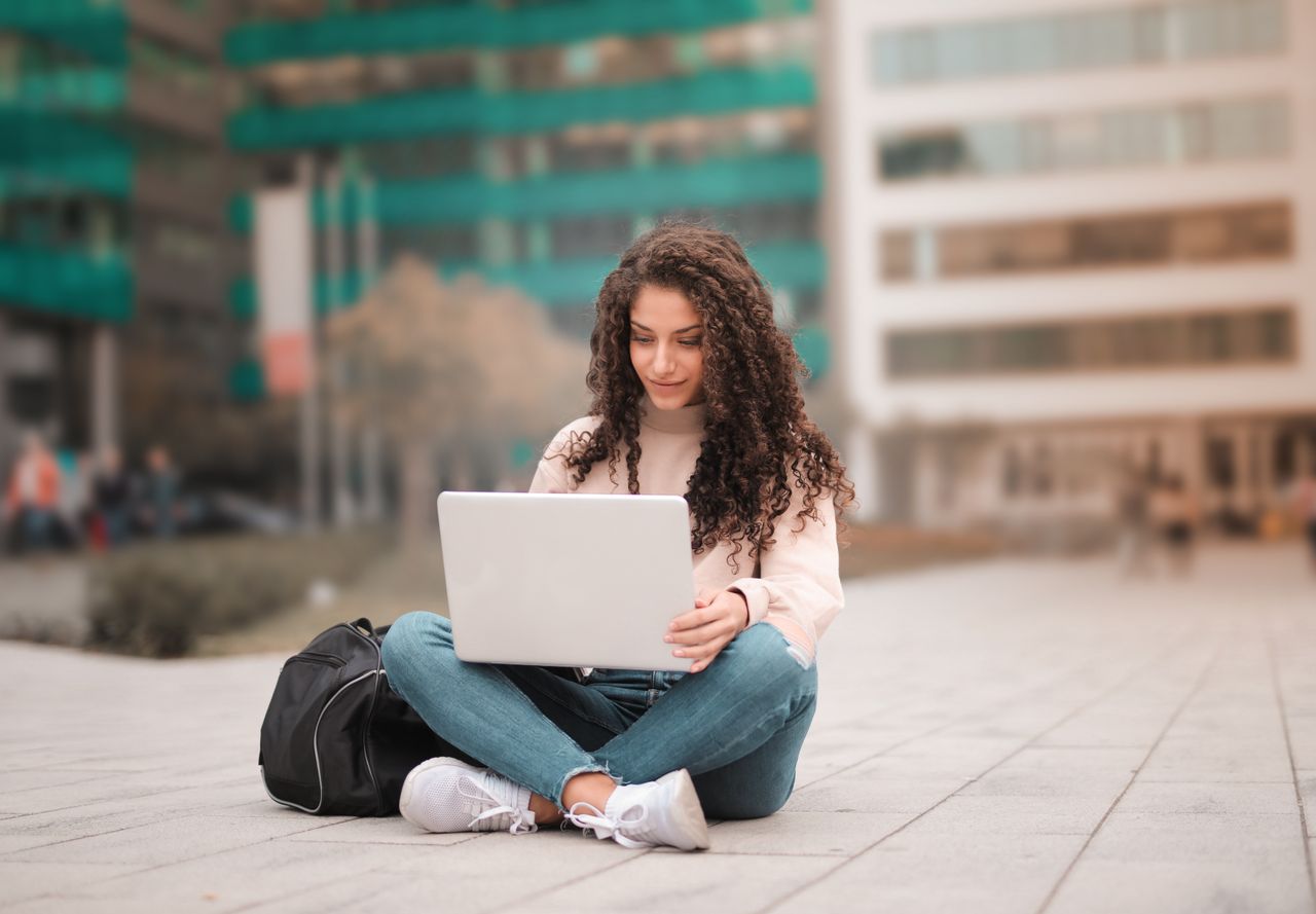 A female student using a laptop while sitting outdoors.
