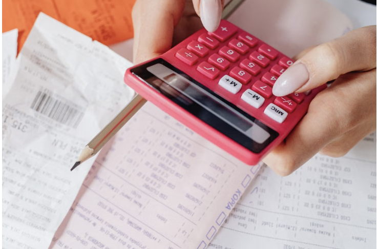 Hands using a red calculator surrounded by financial documents and receipts, symbolizing pricing and financial management.