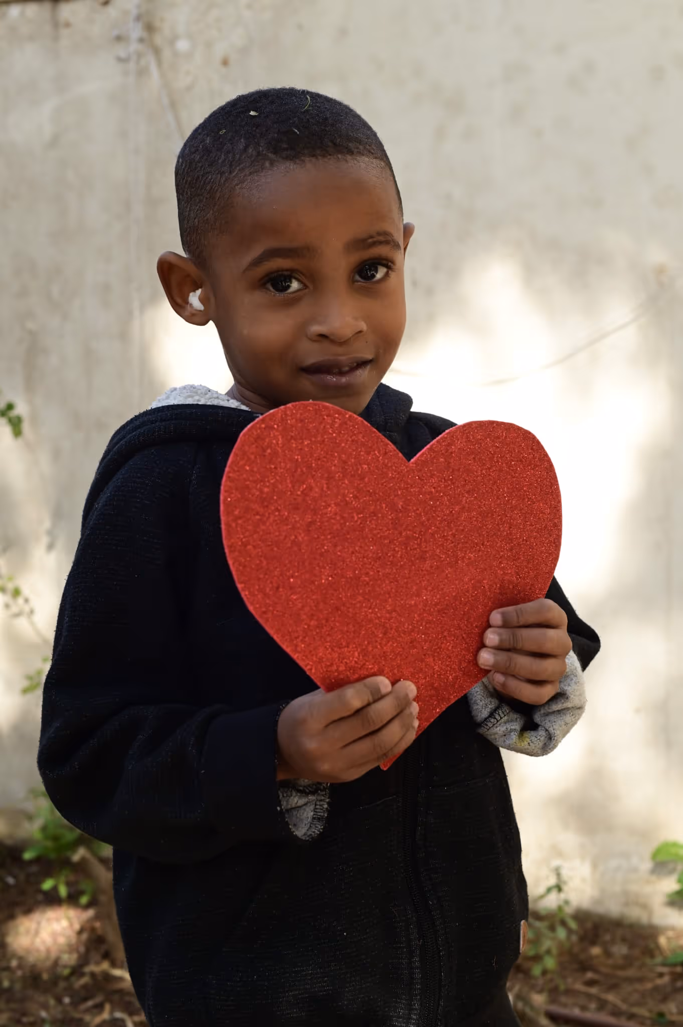 A young boy holding a red heart in his hands.