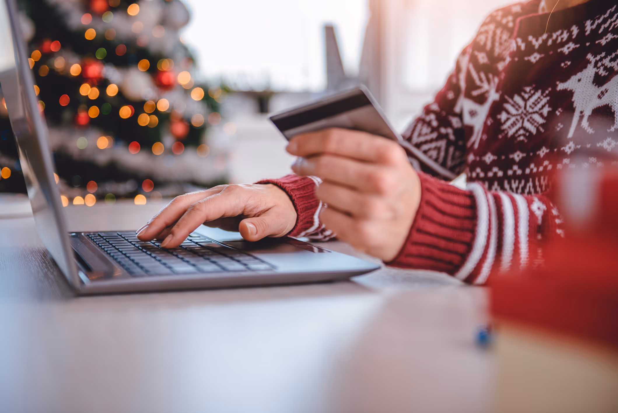 Close up shot of a person's hands working at a laptop with a credit card in their hand