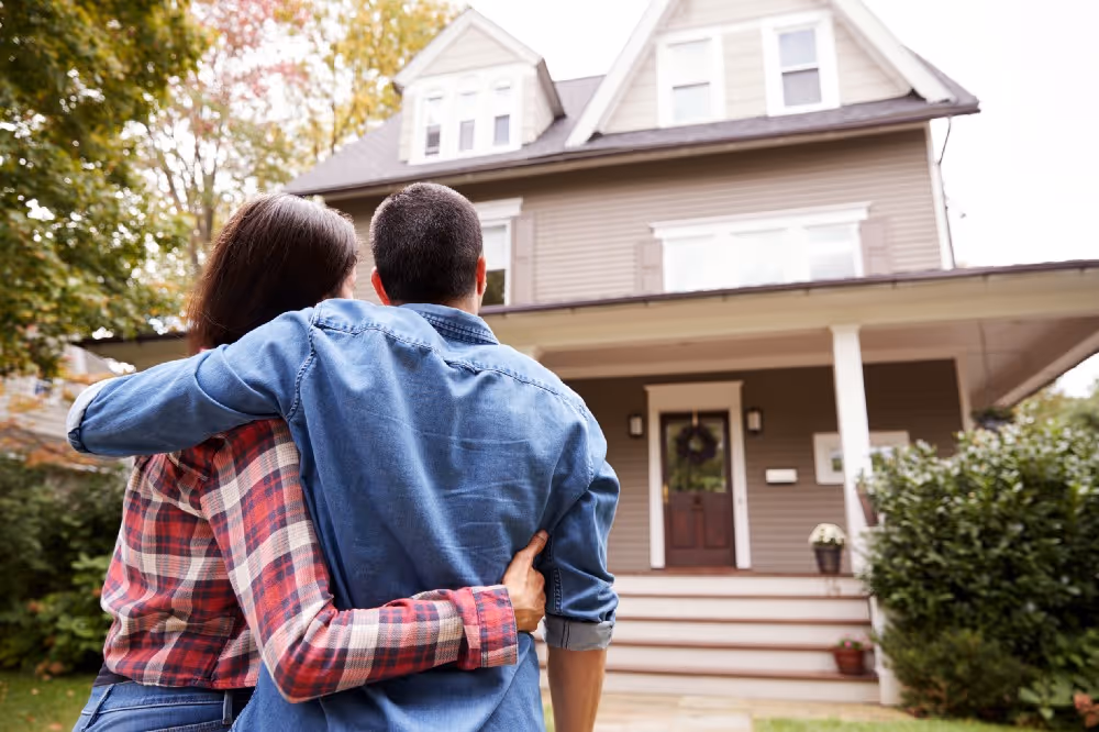 Couple embraces and looks at their home from the front yard