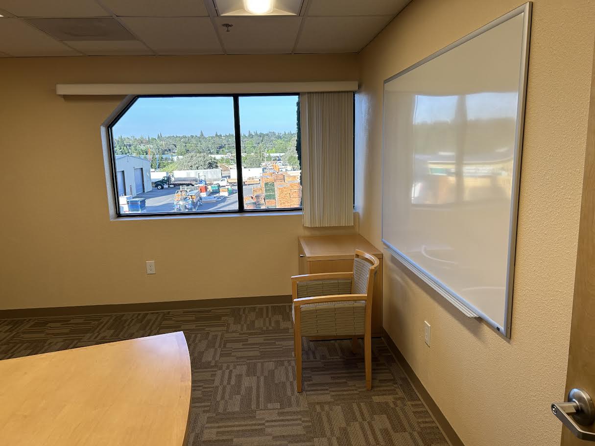 An image of Atwood Business Park's Suite 213 from the Door facing the window with a whiteboard on one side and the corner of a desk on the other. 