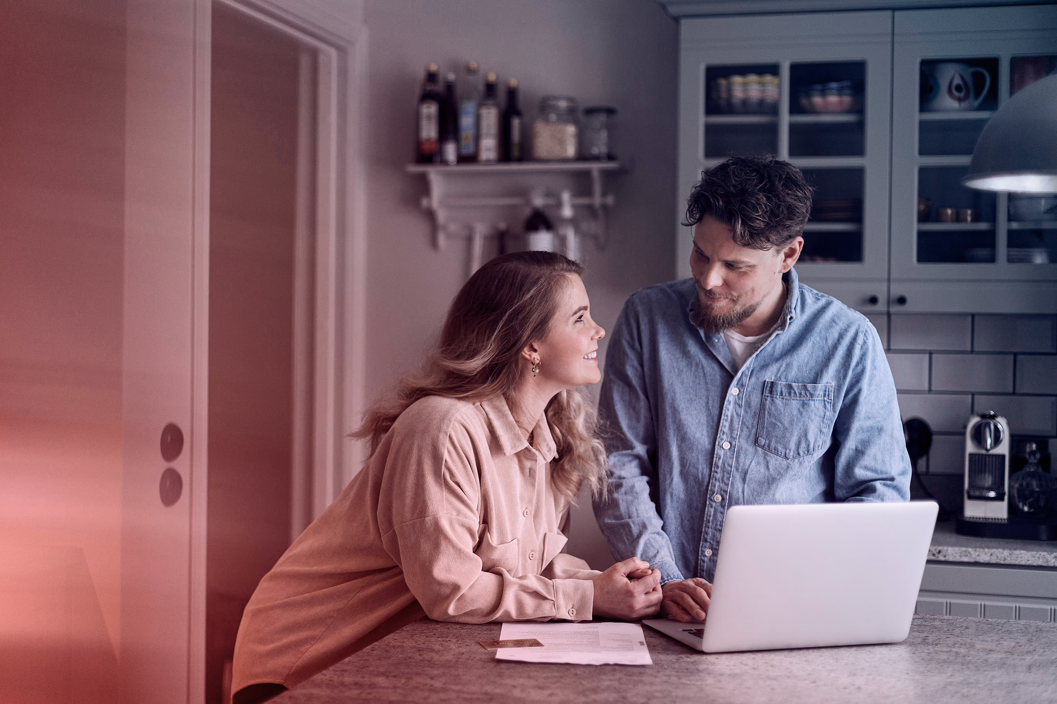 Koppel in keuken praat en lacht terwijl ze samen naar een laptop kijken.