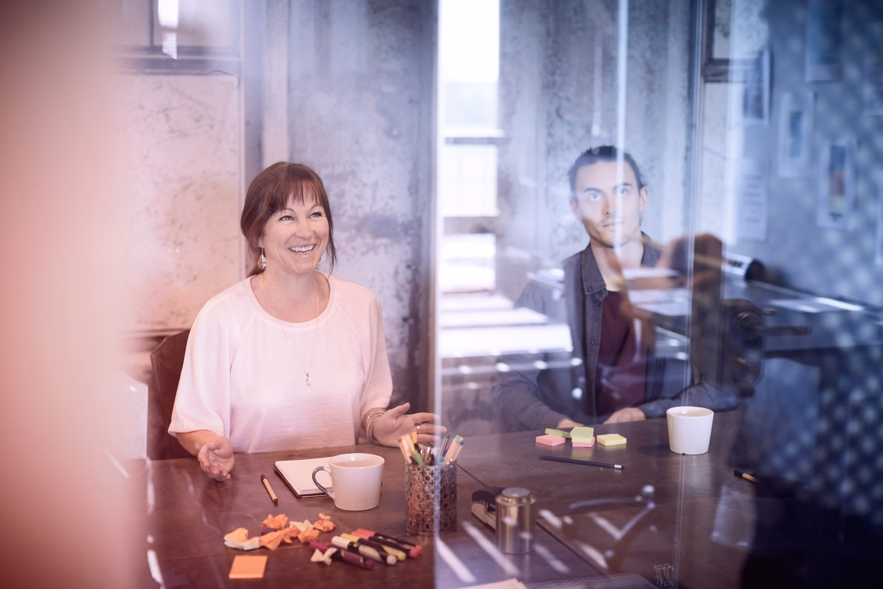Vrouw lacht in vergadering met man die aandachtig luistert in moderne kantoorruimte.
