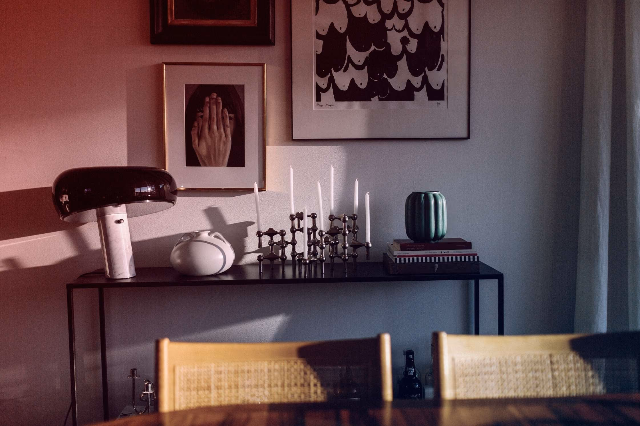 Woonkamerconsole met designlamp, kaarsenstandaard, keramische vaas en kunst aan de muur.