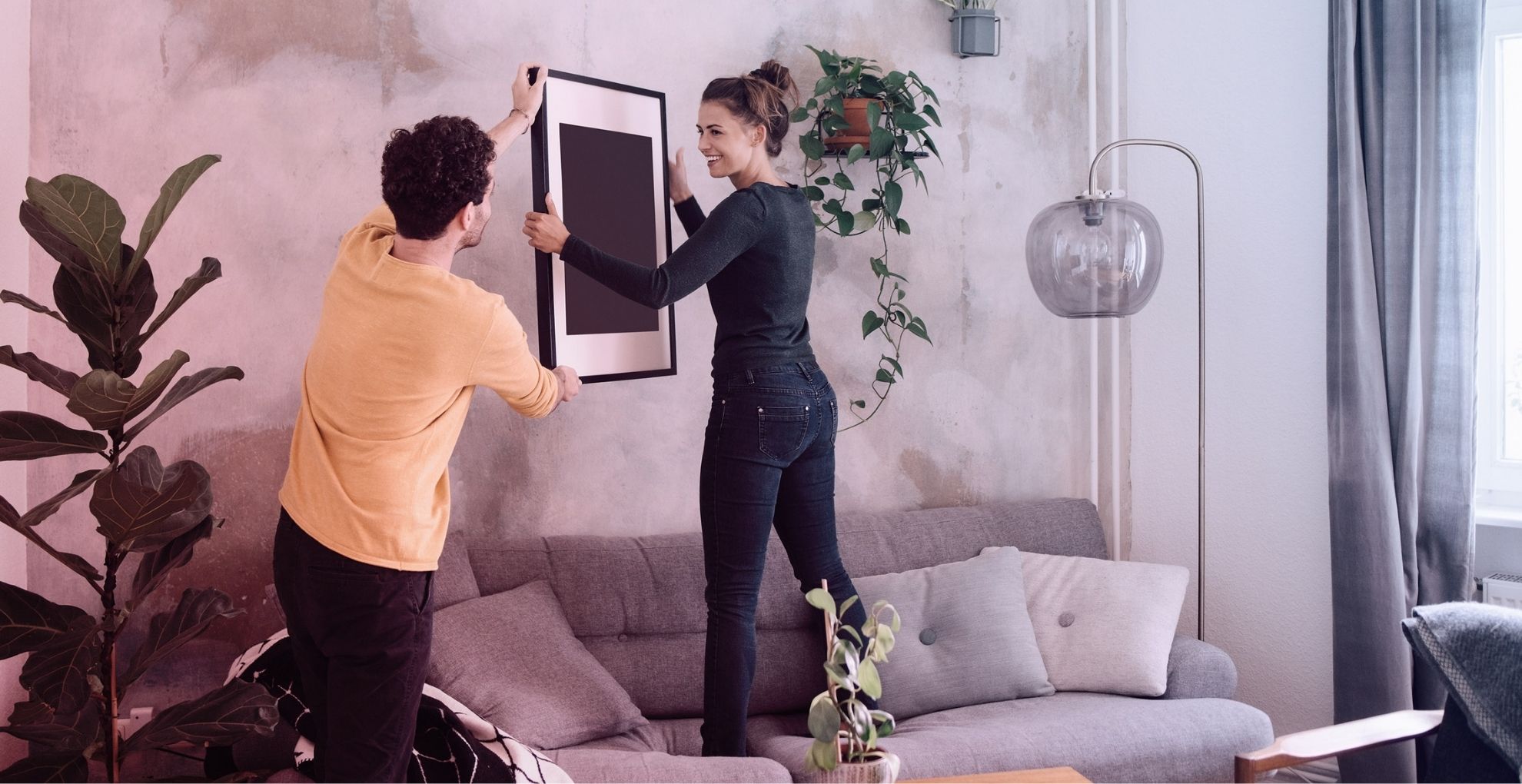Man en vrouw hangen schilderij op in woonkamer