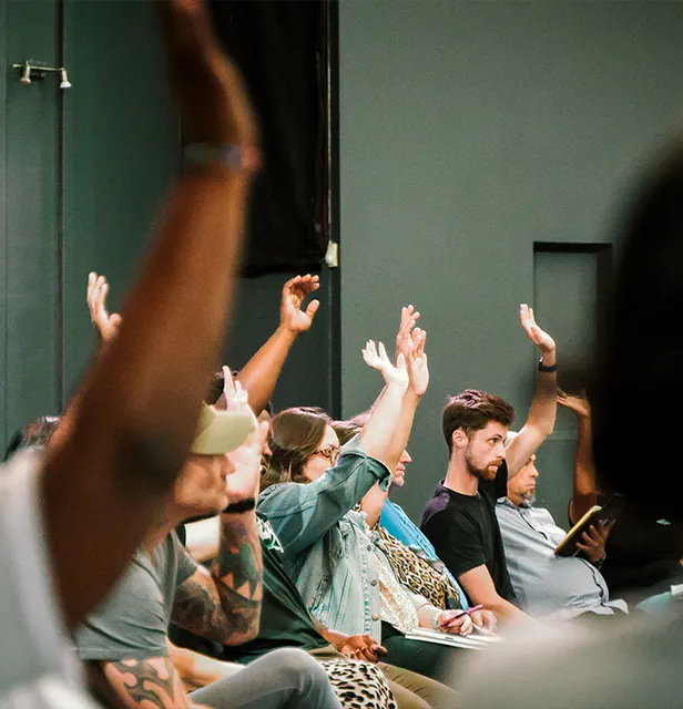 A group of people sitting in a room, all raising their hands in a show of enthusiasm or participation.