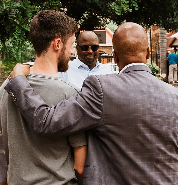 a group of men standing together having a conversation. One man's hand is over another man's shoulder.