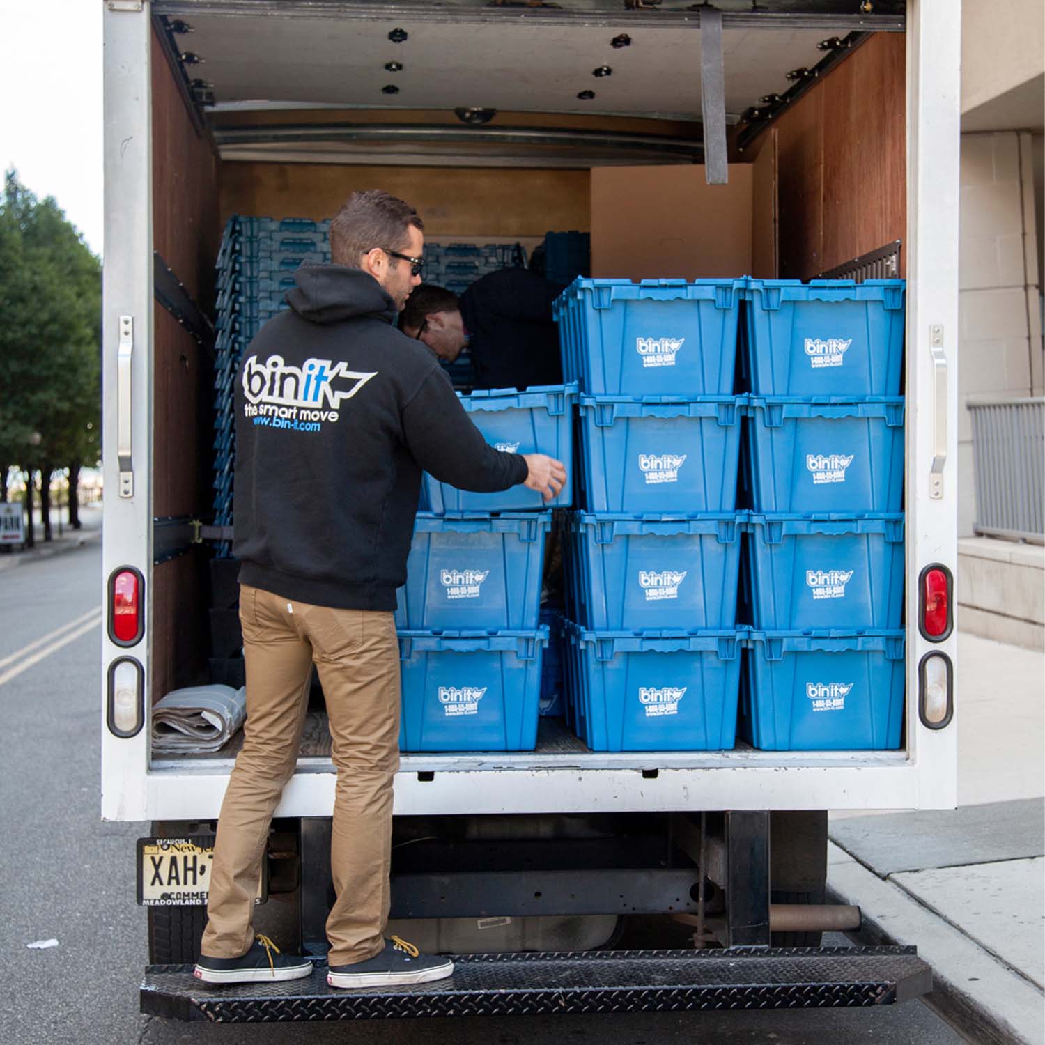 Bin It team member in a Bin It hoodie stacking blue bins inside a moving truck